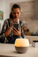 Woman browsing on phone enjoying aromatherapy from essential oil diffuser. Aroma health essence, welness aromatherapy home spa fragrance tranquil theraphy, therapeutic steam, mental health treatment photo