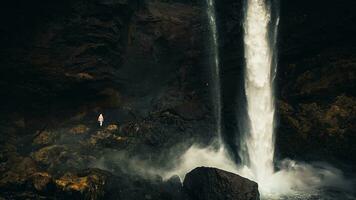 Female tourist walk on pathway visit famous Kvernufoos waterfall landmark. Yellow grass hills on Kvernufoss waterfall. Majestic summer view of pure water river in Iceland, Europe photo