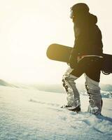 snowboarder caminando con snowboard durante la puesta de sol en las montañas nevadas. fondo cinematográfico de snowboarder freerider en solitario foto