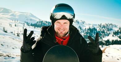 Close up portrait caucasian man with the reflection of snowed mountains, white slope and ski resort. A mountain range reflected in the ski mask. Portrait of man at the ski resort photo