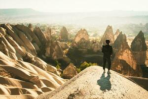 Thoughtful Female person stand look over dramatic valley on hazy morning sunrise with fairy chimneys background. Solo exploration in Turkey photo