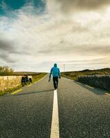 Back view male cyclist in blue jacket walk on road by touring bicycle travel outdoors in Ireland. Purpose and travel adventure concept. Wild atlantic way road trip photo