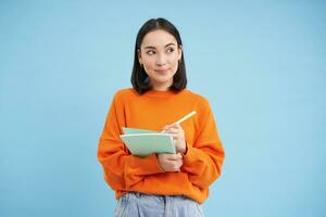 Education and students. Happy asian woman, holding notebooks and laughing, smiling at camera, enjoys going to University or College, blue background photo