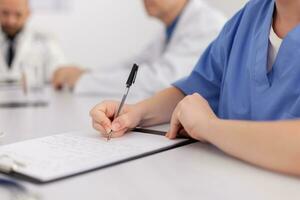 Closeup of woman nurse hands writing sickness treatment on clipboard working at healthcare medical expertise sitting at desk in conference meeting room. Physician asisstant analyzing pills medication photo