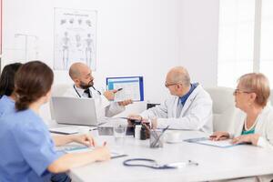 Practitioner doctor showing medical expertise presentation on clipboard discussing sickness diagnosis with teamwork working at healthcare treatment. Physiotherapists sitting at desk in meeting room photo