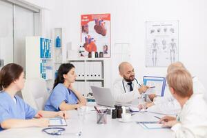 Physiotherapist man doctor holding clipboard in hands presenting healthcare expertise explaining sickness treatment discussing disease diagnostic. Practitioners teamwork working in meeting room photo