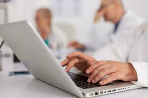 Closeup of therapist doctor hands prescribing pill medication treatment typing sickness expertise on laptop computer. Practitioner man sitting at desk in meeting room analyzing disease diagnosis photo