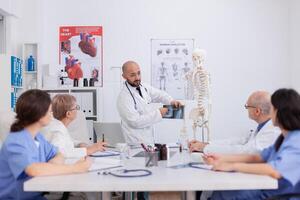 Hospital team discussing body bone structure using medical xray explaining sickness diagnosis. Physician doctor working at healthcare treatment in conference meeting room presenting biology expertise photo