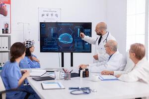 Physician pointing medical radiography to hospital coworkers analysing brain sickness presentation using high tech in meeting room. Hospital team monitoring ill treatment for healthcare expertise photo