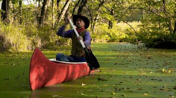 A cowboy in a red canoe floats on green river in the forest. Historical reconstruction of life in the wild west of America. photo