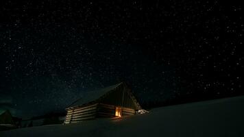 Stars in the night sky and a wooden house with a glowing window in winter photo