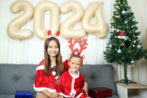 alegre Navidad 2024 concepto madre y niño Decorar el Navidad árbol con vistoso Navidad pelotas. foto