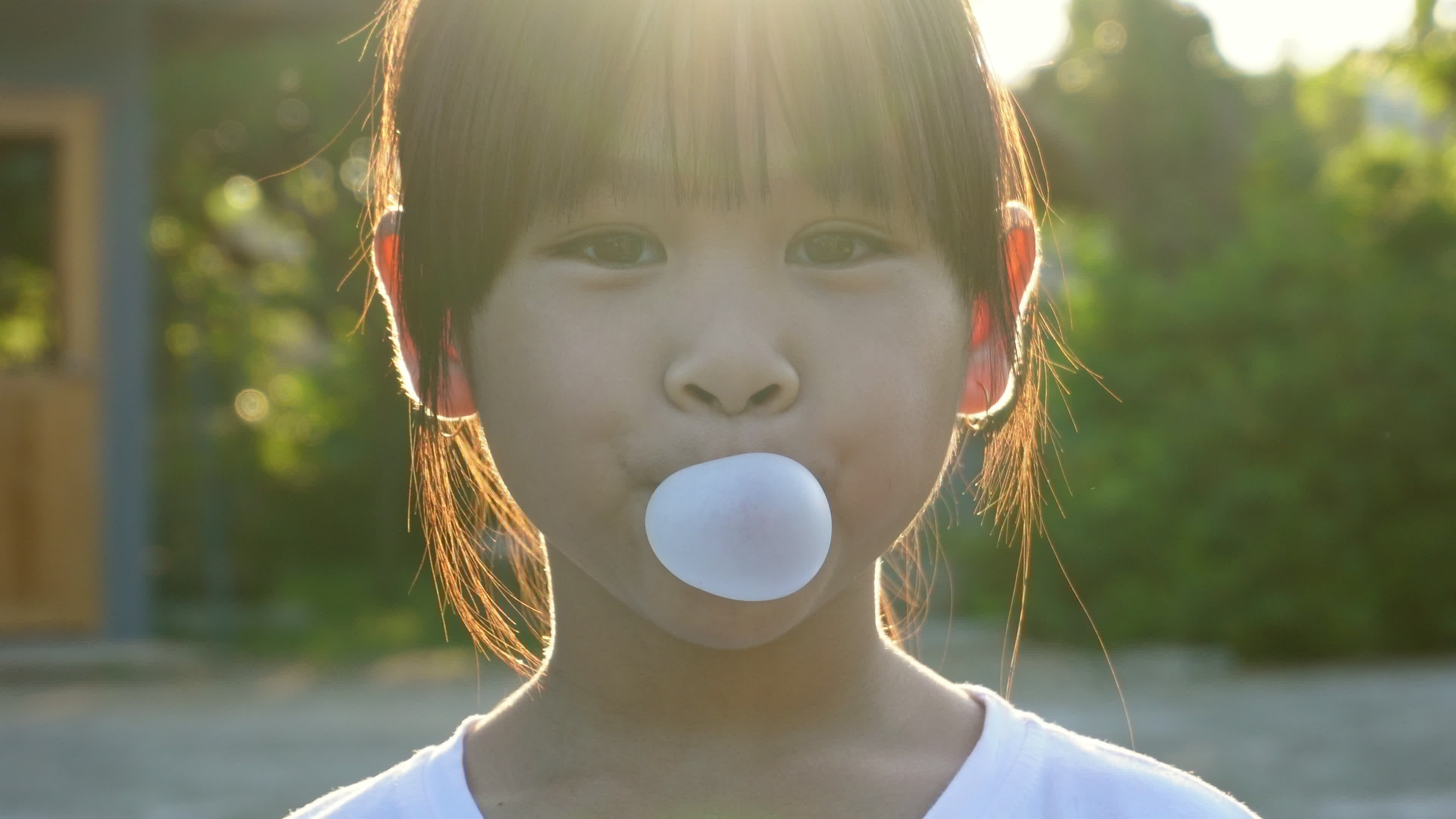 Cute little girl enjoys eating chewing gum and blowing bubbles in the