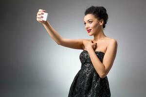 Portrait of a Beautiful successful smiling girl doing selfie in black dress on light background photo