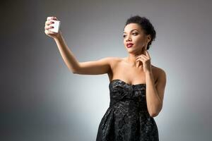 Portrait of a Beautiful successful smiling girl doing selfie in black dress on light background photo