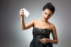 Portrait of a Beautiful successful smiling girl doing selfie in black dress on light background photo