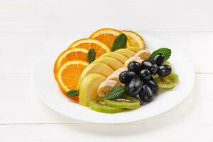 Slices of orange, banana, kiwi, apple and grape on plate photo