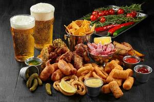 Two glasses of beer with savory snacks and vegetables on black photo