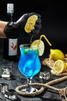 Male hand in glove squeezing lemon into glass with Blue Lagoon cocktail photo