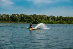 Sporty man riding on wakeboard on river on summer day photo