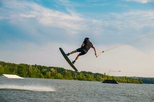 joven hombre saltando terminado agua superficie de río en wakeboard foto