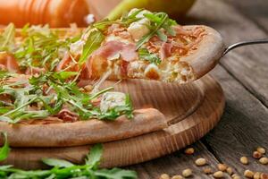 Slice of pizza with cured ham, blue cheese, pear, pine nuts, arugula photo