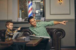 Young father and his stylish little son in the barbershop in the waiting room. photo