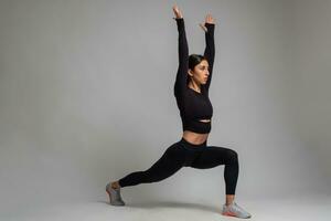 Girl doing forward lunges with arms stretched upwards on grey background photo