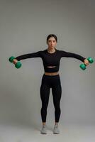 Sporty girl performing dumbbell lateral raise on grey background photo