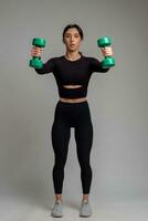 Girl performing shoulder exercises with dumbbells on grey background photo