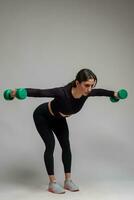Athletic girl doing shoulders exercises with dumbbells on grey background photo