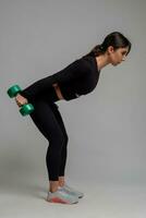 Sporty girl performing triceps kickback with dumbbells on grey background photo