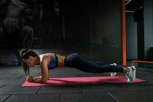 Focused young woman keeping plank pose on elbows in gym photo