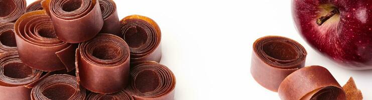 Rolls of fruit leather and apple on white surface photo