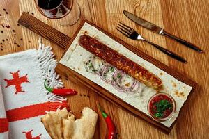 Chicken lula kebab on wooden table with lavash, onions, greens and satsebeli photo