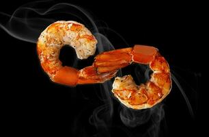 Two grilled shrimp tails in shape of infinity sign on black photo