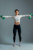Athletic girl performing dumbbell lateral raise on grey background photo