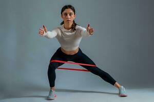 Woman performing lateral lunges with resistance band on grey background photo