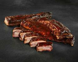 Sliced grilled pork ribs in barbecue sauce on stone surface photo