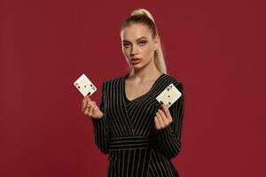 rubia mujer en negro vestir en pedrería. demostración dos jugando tarjetas, posando en contra rojo antecedentes. juego entretenimiento, póker, casino. de cerca foto