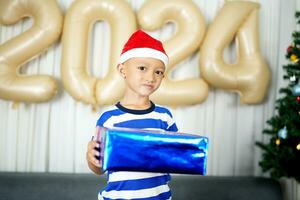 Merry Christmas 2024 concept A boy holding a gift box is happy to receive a present on Christmas Day. photo