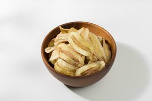 Banana chips in a wooden bowl on a white table photo