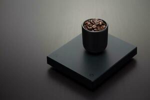 Dark roasted coffee beans in a small black mug on a digital scale. photo