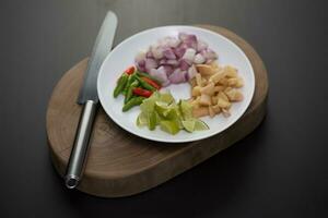 Herbs and sliced vegetables for cooking on a white plate placed on a Wooden cutting board. photo