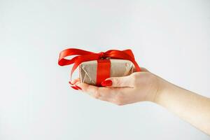 Gift box with red ribbon on white background in hands of a young woman. photo