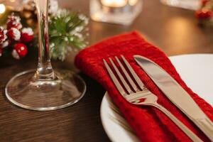 Christmas table setting. Plate and cutlery on napkin. Preparing for festive dinner. Candles burning on table on Christmas Eve. photo