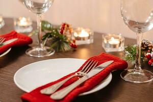 Christmas table setting. Plate and cutlery on napkin. Preparing for festive dinner. Candles burning on table on Christmas Eve. photo