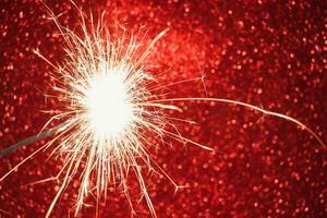 New Year celebration. Sparkler on red background. Christmas night. Bright sparks of fire and bokeh. photo