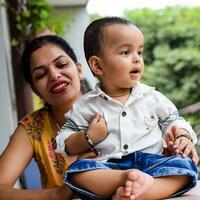 Loving mom carrying of her baby at home balcony. Bright portrait of happy mum holding child in her hands. Mother with her little 1 year old son. photo