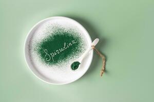 Beautiful spirulina lettering of natural green seaweed powder on a white ceramic plate. Top view. green background. Healthy supplements photo